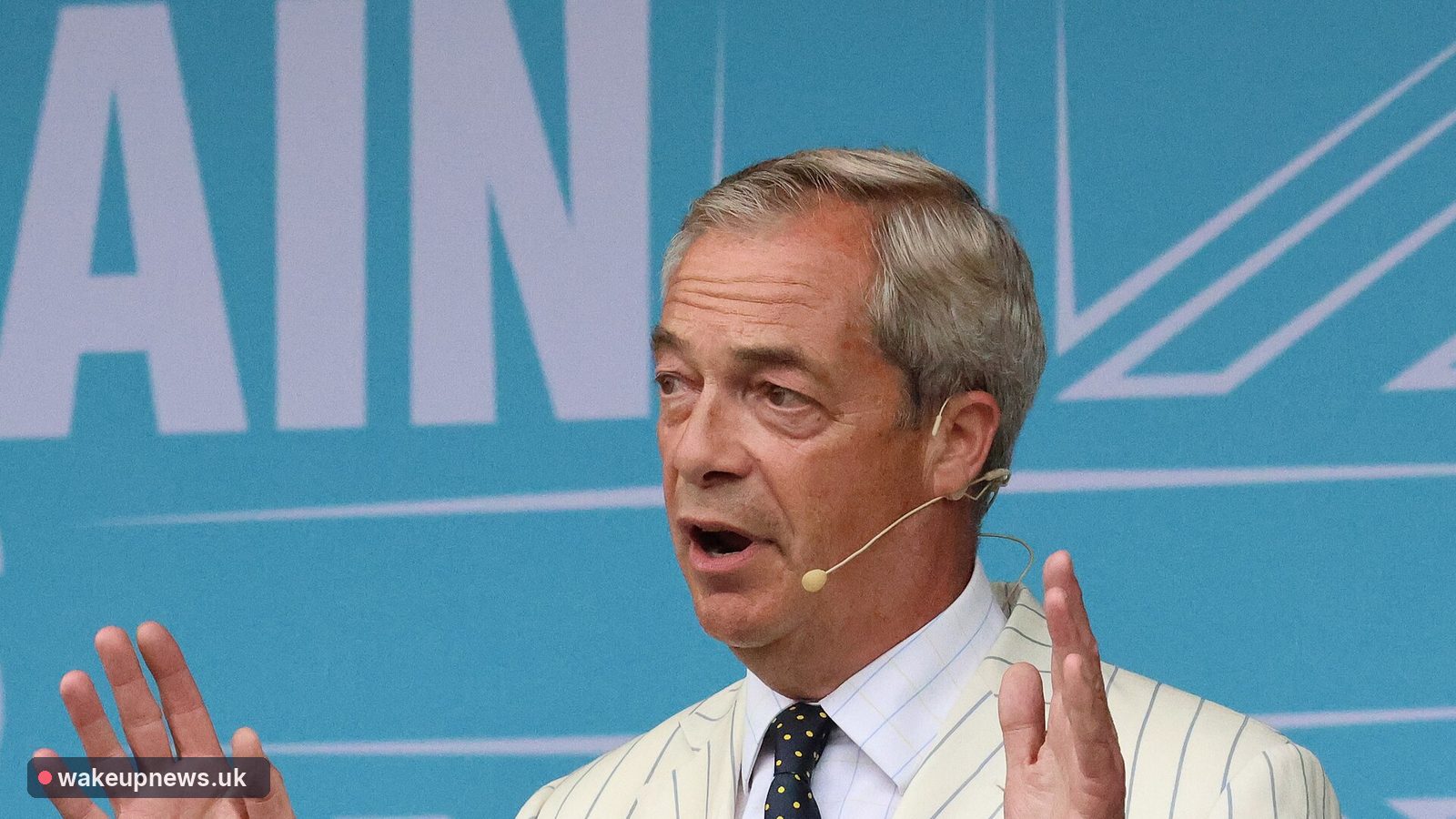 Nigel Farage in a striped jacket speaking at a Reform UK rally