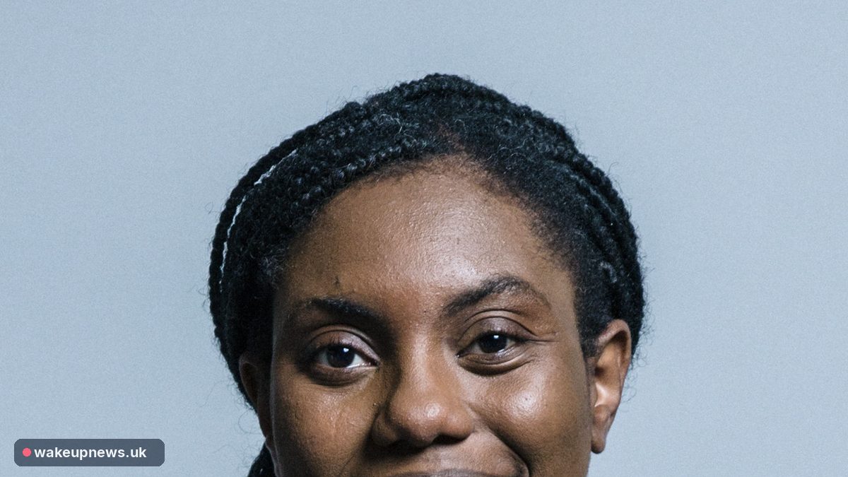Head-and-shoulders portrait of Kemi Badenoch smiling against a plain grey background