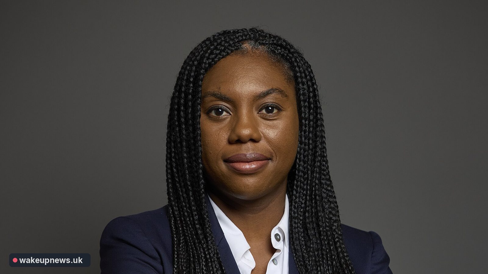 Kemi Badenoch in a navy jacket and white shirt against a grey background