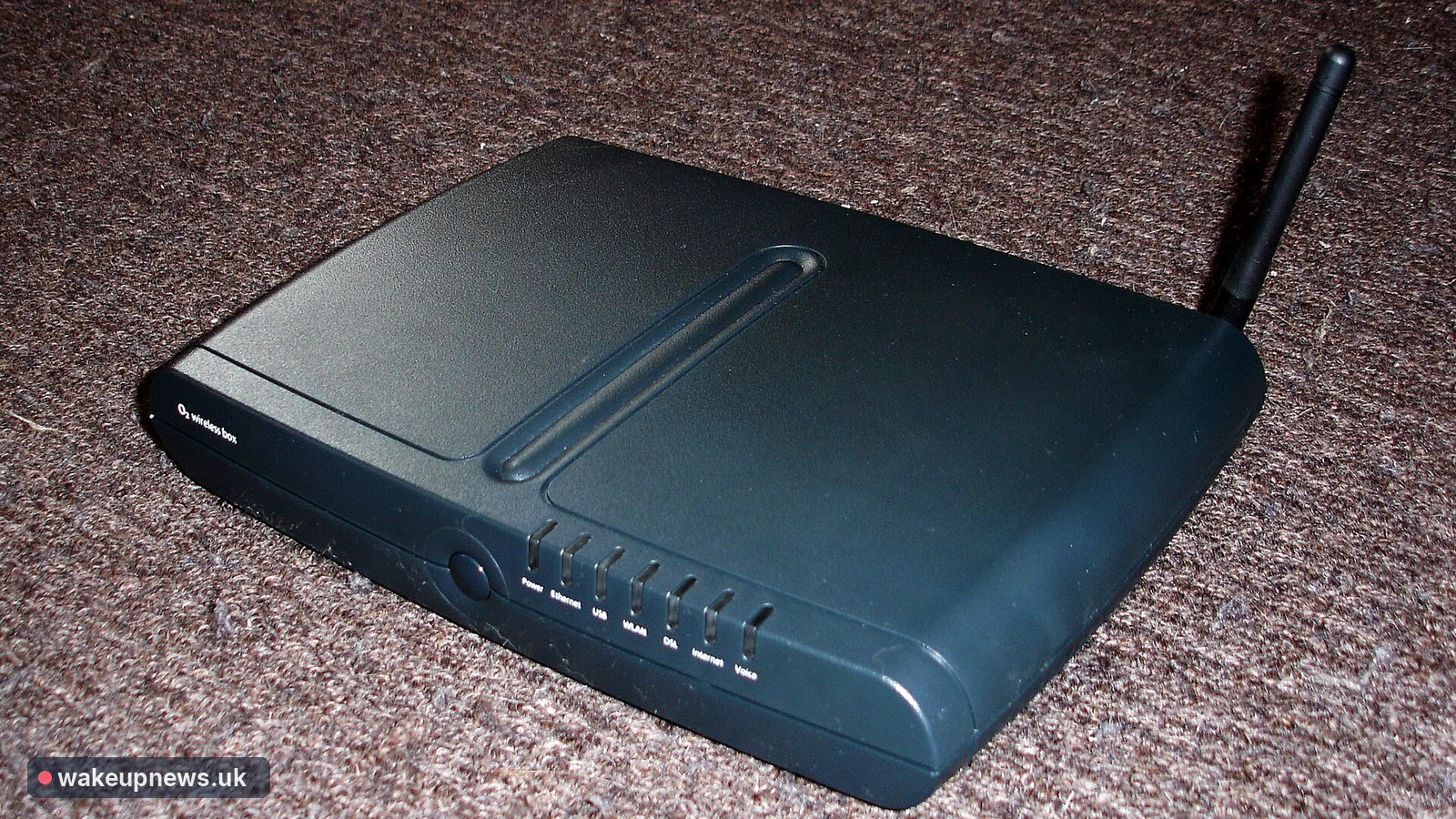 Black home broadband router with an aerial resting on a brown carpet